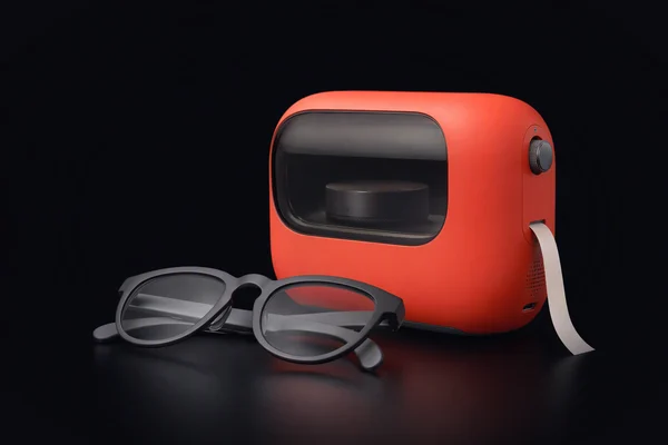 Plain display glasses folded in front of a sealed red compute cell with a smoked-glass window showing a small puck inside, a strip of paper tape feeding out of its side